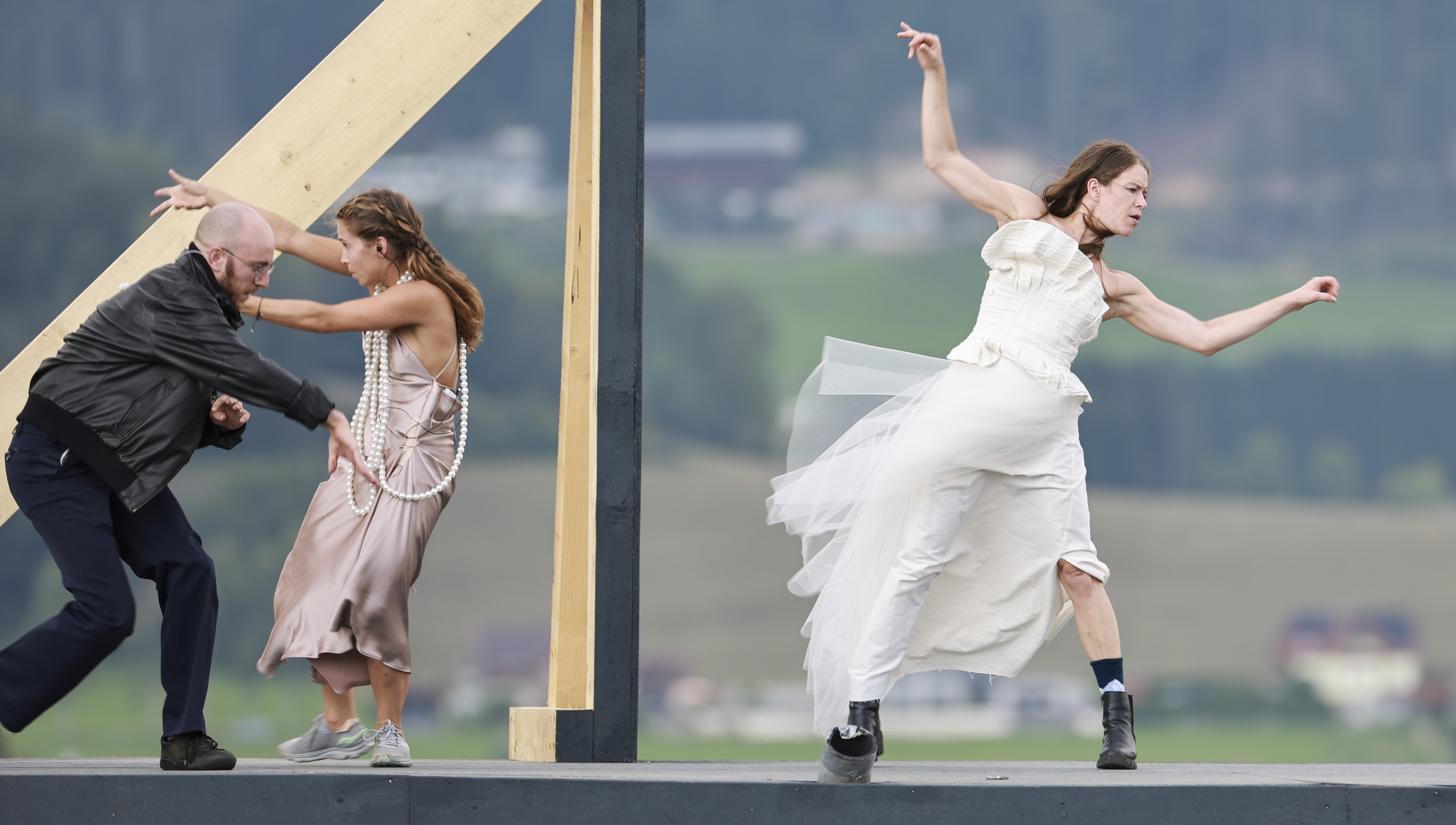 Drei Personen führen auf einer Freilichtbühne zeitgenössischen Tanz auf; eine in einem weißen Kleid, eine in rosa und eine in dunkler Kleidung.