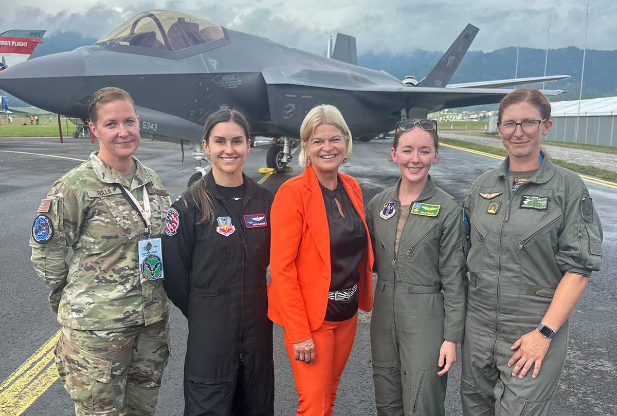 Fünf Frauen, vier in Militäruniformen, stehen an einem bewölkten Tag gemeinsam vor einem Kampfjet.